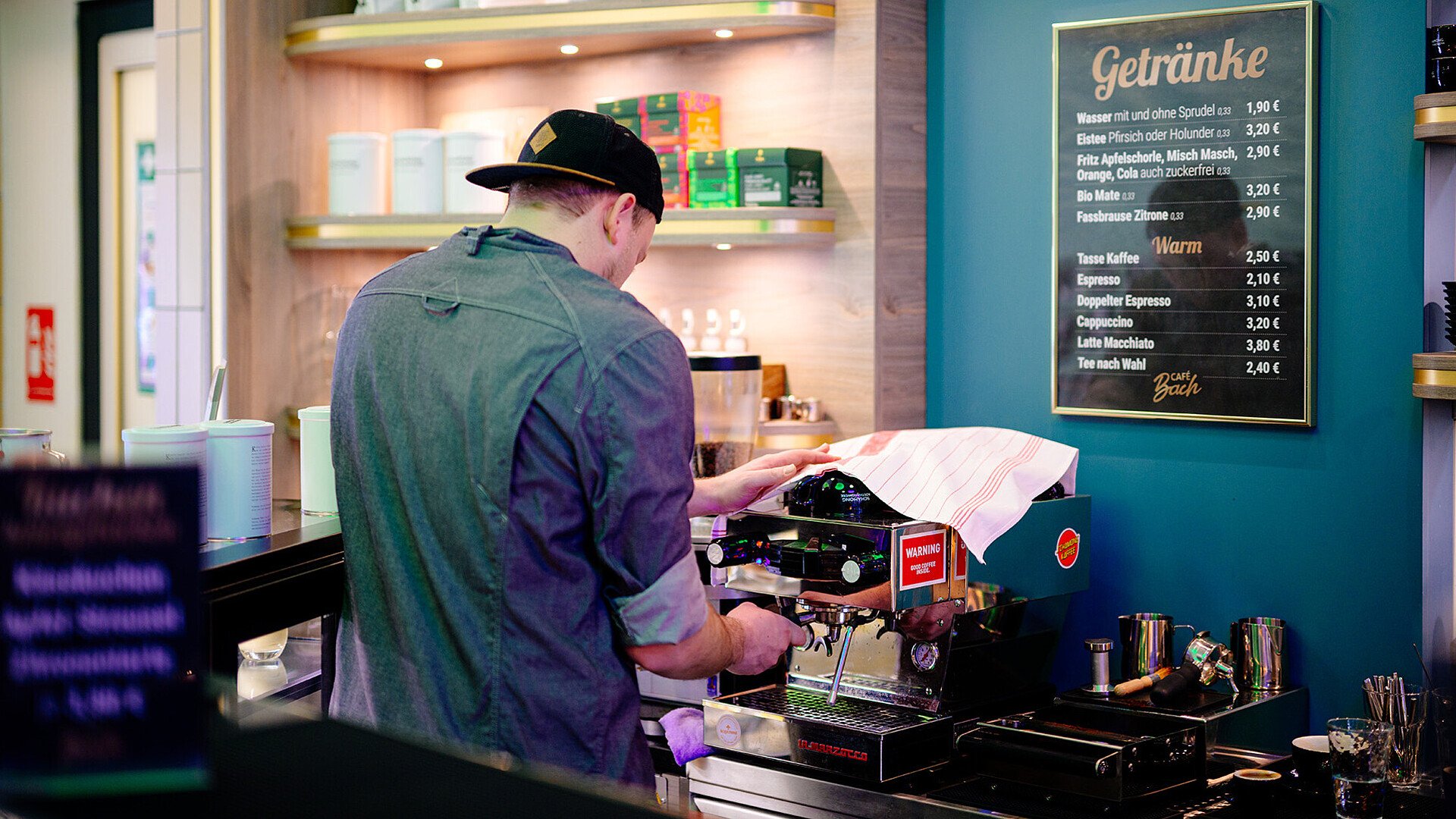 Ein Mitarbeiter des Café Bachs in der Kölner Altstadt bereitet ein Getränk am Kaffeeautomaten zu