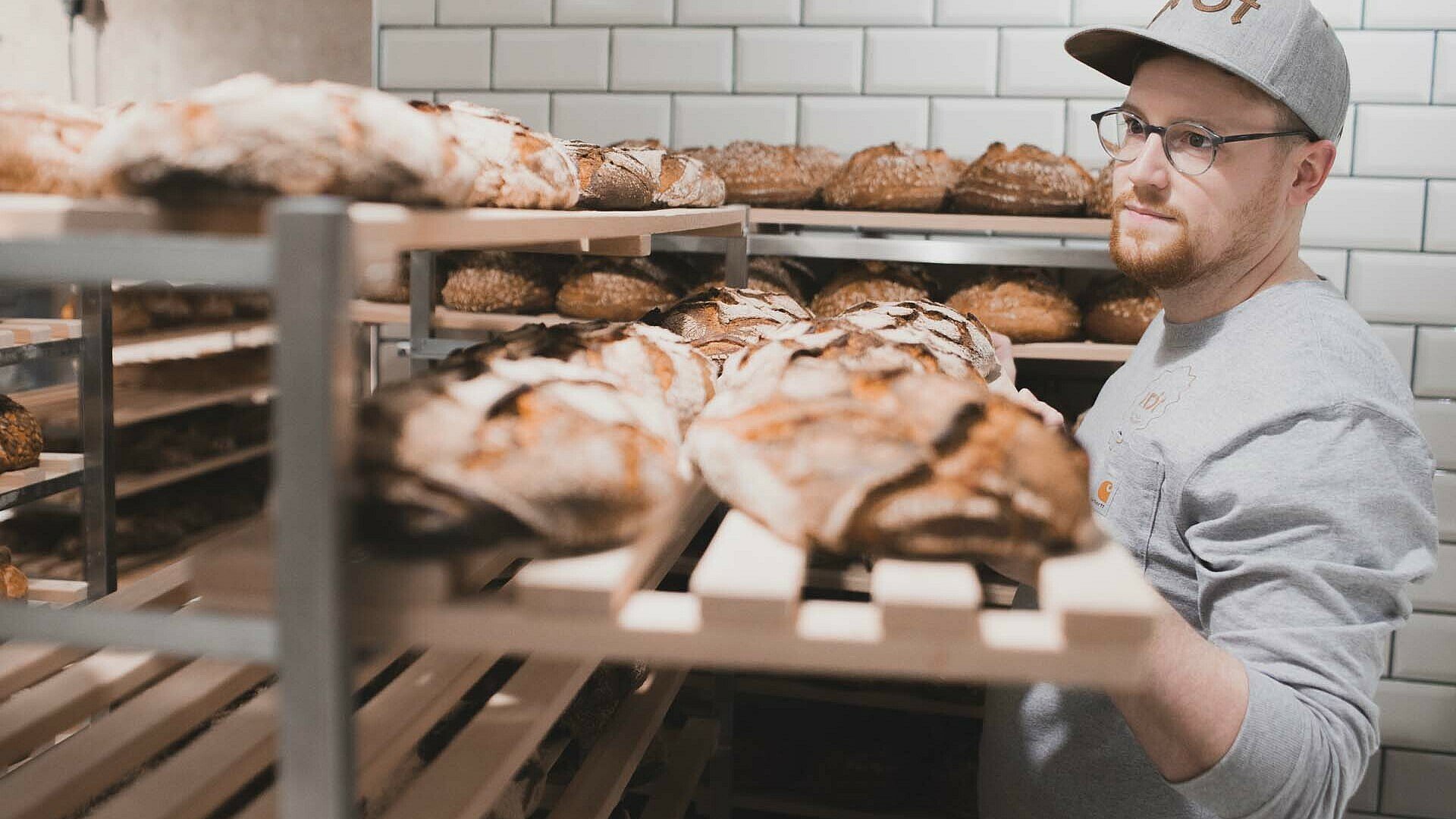 Alex Onasch schiebt in seiner Bäckerei prôt im Belgischen Viertel in Köln ein Brett mit Broten auf ein Regal 