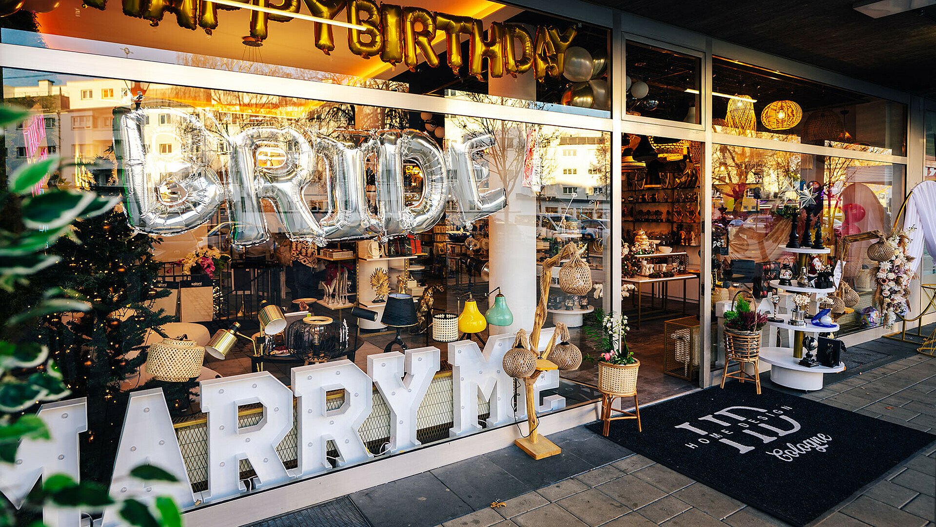 Die Schaufenster von HD Home Design in Buchforst mit dem leuchtenden Schriftzug „Marry Me“ und einem Ballon mit Schriftzug „Bride“