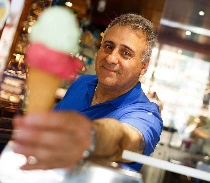 Der Besitzer vom Eiscafé Gioia in Niehl reicht ein Eis über die Theke