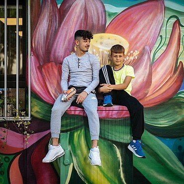 David und Julian vor einem Blumenmotiv der neuen Außenfassade des Jugendzentrums Fzwei.
