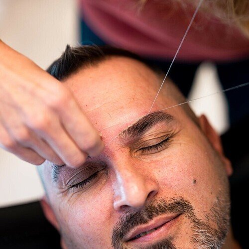 Inhaberin Nuran Altinok zupft die Augenbrauen eines Kunden im Friseursalon Coiffeur Nora in der Kölner Südstadt