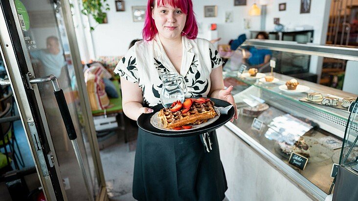 Eine Kellnerin serviert Sorbet und Törtchen im Café Alte Wäscherei in Zollstock