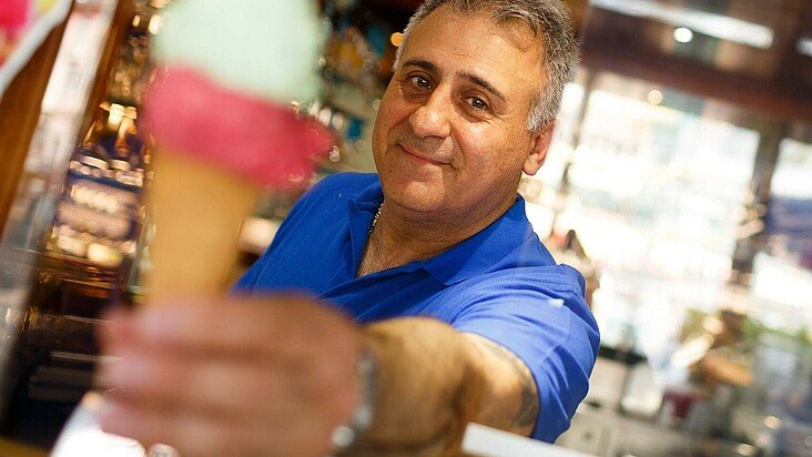 Der Besitzer vom Eiscafé Gioia in Niehl reicht ein Eis über die Theke