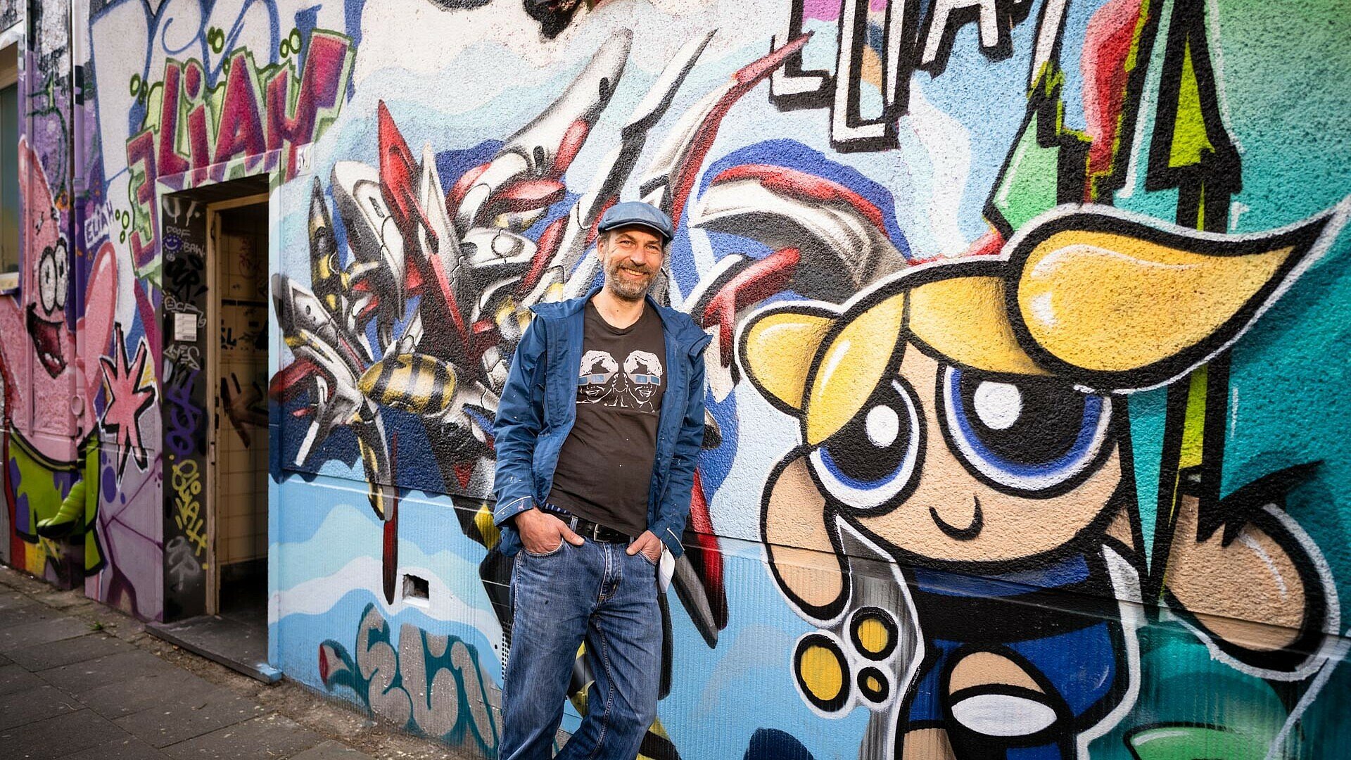 Künstler Adrian Savulescu vor einer Wand voller Graffitis in Köln-Kalk